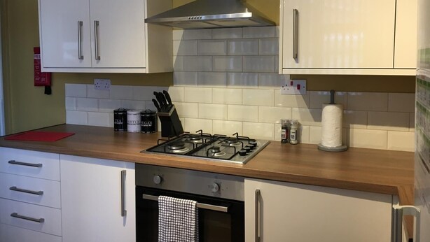 A kitchen with white cabinets, a gas stove, a stainless steel range hood, and a red fire extinguisher. - Brooklyn Place (Crewe)
