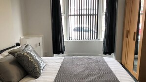 A bedroom with a bed, a radiator, a window with blinds, and a wardrobe. - Brooklyn Place (Crewe)