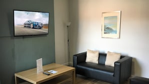 A modern living room with a wooden coffee table, a black leather sofa, a television mounted on the wall, and a framed painting on the wall. - Brooklyn Place (Crewe)