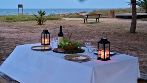 An outdoor dining setup with a table, lanterns, and a bottle of wine on a beach. - Pinea Mare (Poggio-Mezzana)