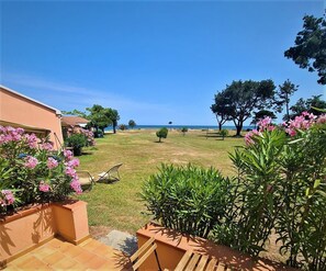 A patio area with a view of the sea, surrounded by greenery and a building with a tiled floor.