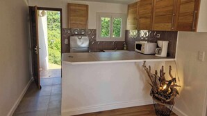 A modern kitchen with wooden cabinets, a central island, and a view of greenery outside. - Pinea Mare (Poggio-Mezzana)