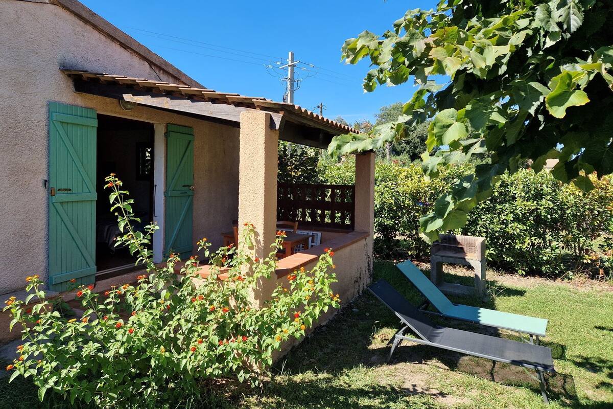 A house with a covered porch, a lawn, and a lounge chair.