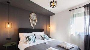 A neatly made bed with white and grey linens, a dreamcatcher decoration, and a bedside table with a remote control. - Villa Royal with heated pool and sauna (Biograd na moru)