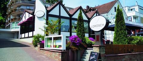 A hotel named 'LOROSCH' with a traditional European architectural style, featuring a prominent clock and a signboard.