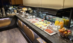 A buffet with a variety of food items and beverages, including fruits, cheeses, and meats, displayed on a marble counter.