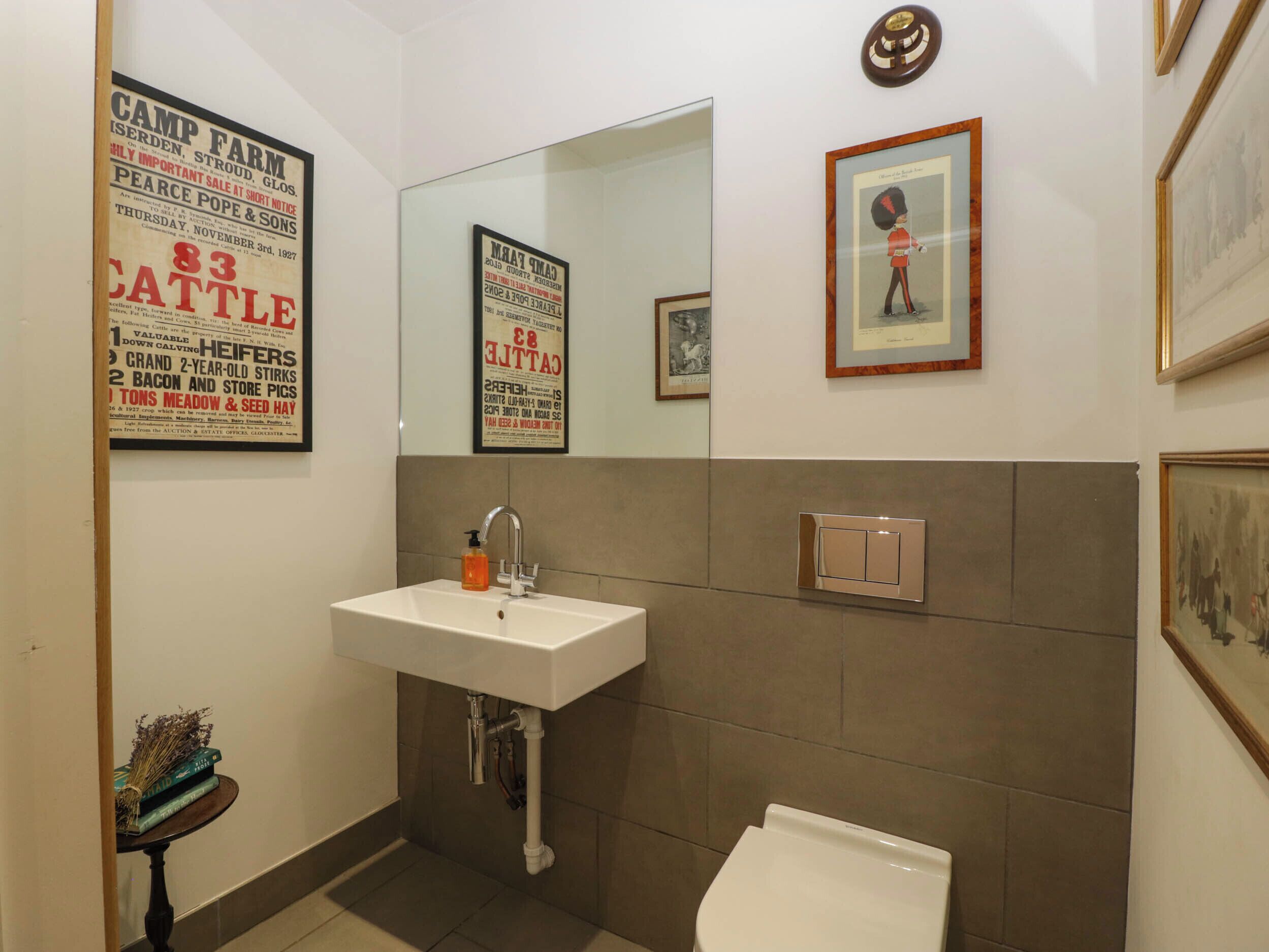 A bathroom with a white sink, a mirror, a framed picture of a guard, and a poster advertising cattle.