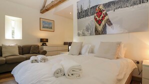 Ein Schlafzimmer mit einem großen Bett, einem Schlafsofa, einem Nachttisch und einem Gemälde einer verschneiten Landschaft.