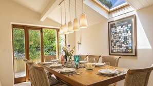 A dining area with a wooden table, wicker chairs, hanging pendant lights, and a framed family tree on the wall. - Higher Collaton Cottage (Kingsbridge)