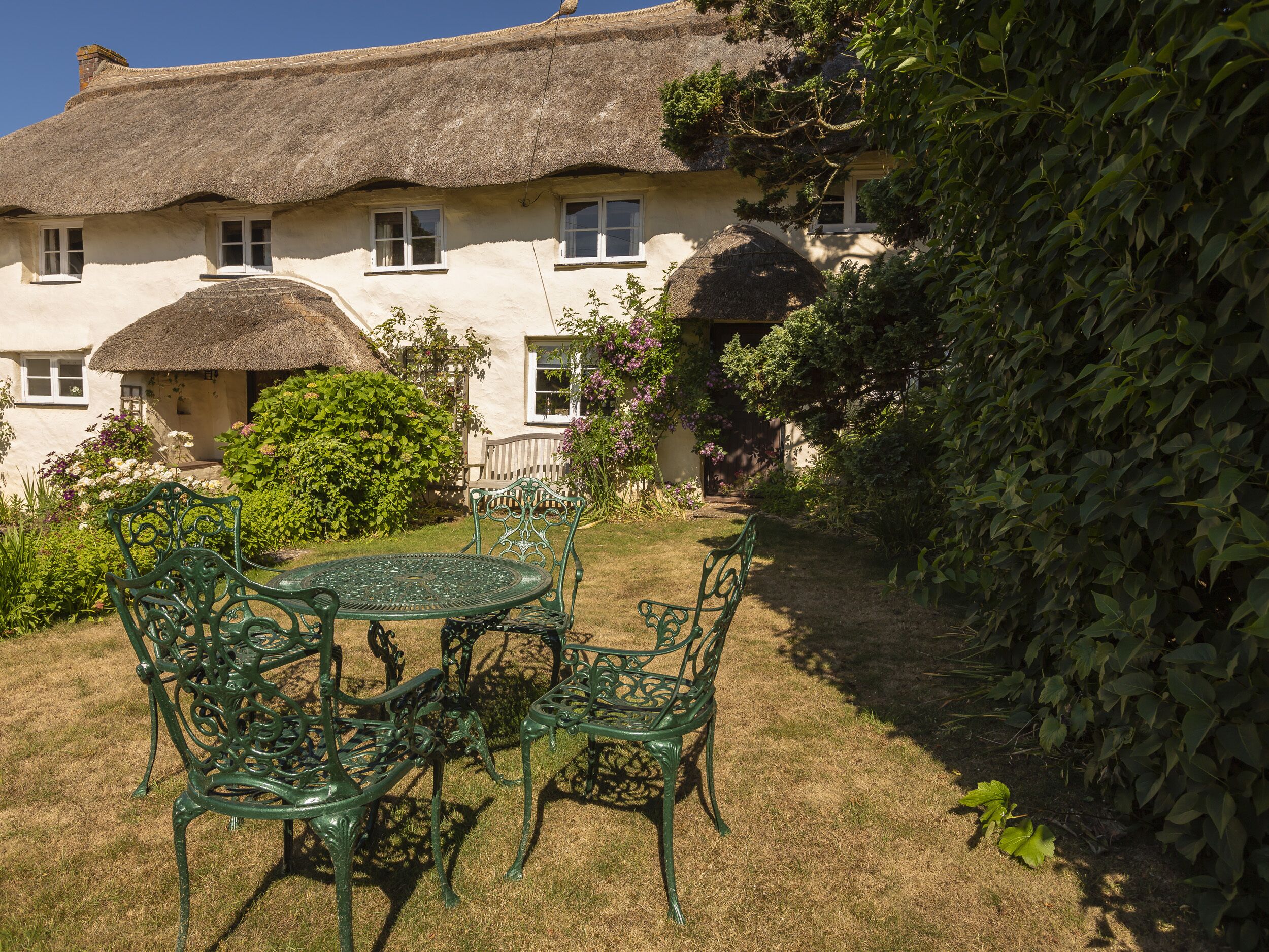 A thatched-roof house with a garden and a round metal table with chairs.