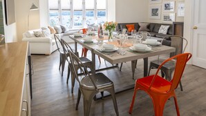 Un espace repas moderne avec une grande table dressée pour six personnes, entourée de chaises, d’un canapé et d’une table basse.
