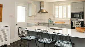 A modern kitchen with white cabinets, a central island with chairs, a stainless steel range hood, and a Bosch oven. - Cindy's Retreat (Kingsbridge)