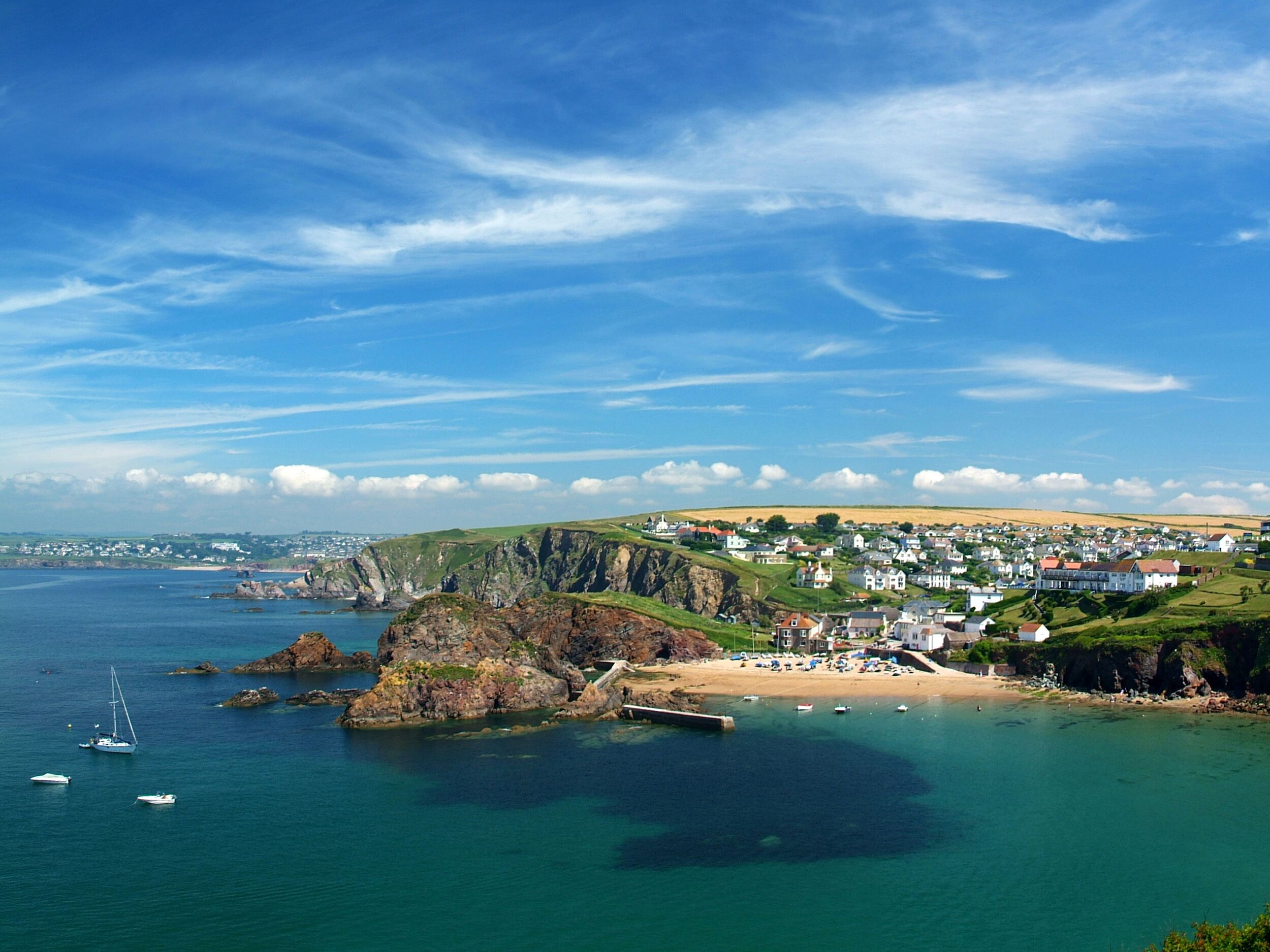A coastal town with a beach, rocky cliffs, and houses.