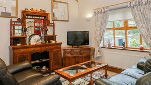 A living room with a sofa, a wooden cabinet, a television, and a window with curtains. - Gelli Glud (Colwyn Bay)