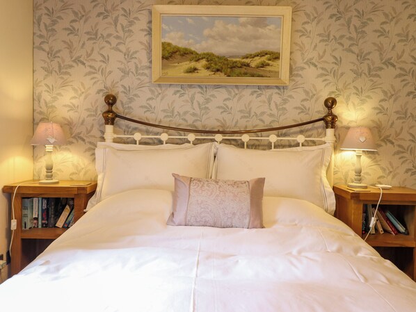 A neatly made bed with a headboard, two bedside lamps, and a bookshelf with books.