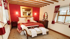 A bedroom with a large bed, a wooden headboard, a mirror, a dresser, and a window with curtains. - Gelli Glud (Colwyn Bay)