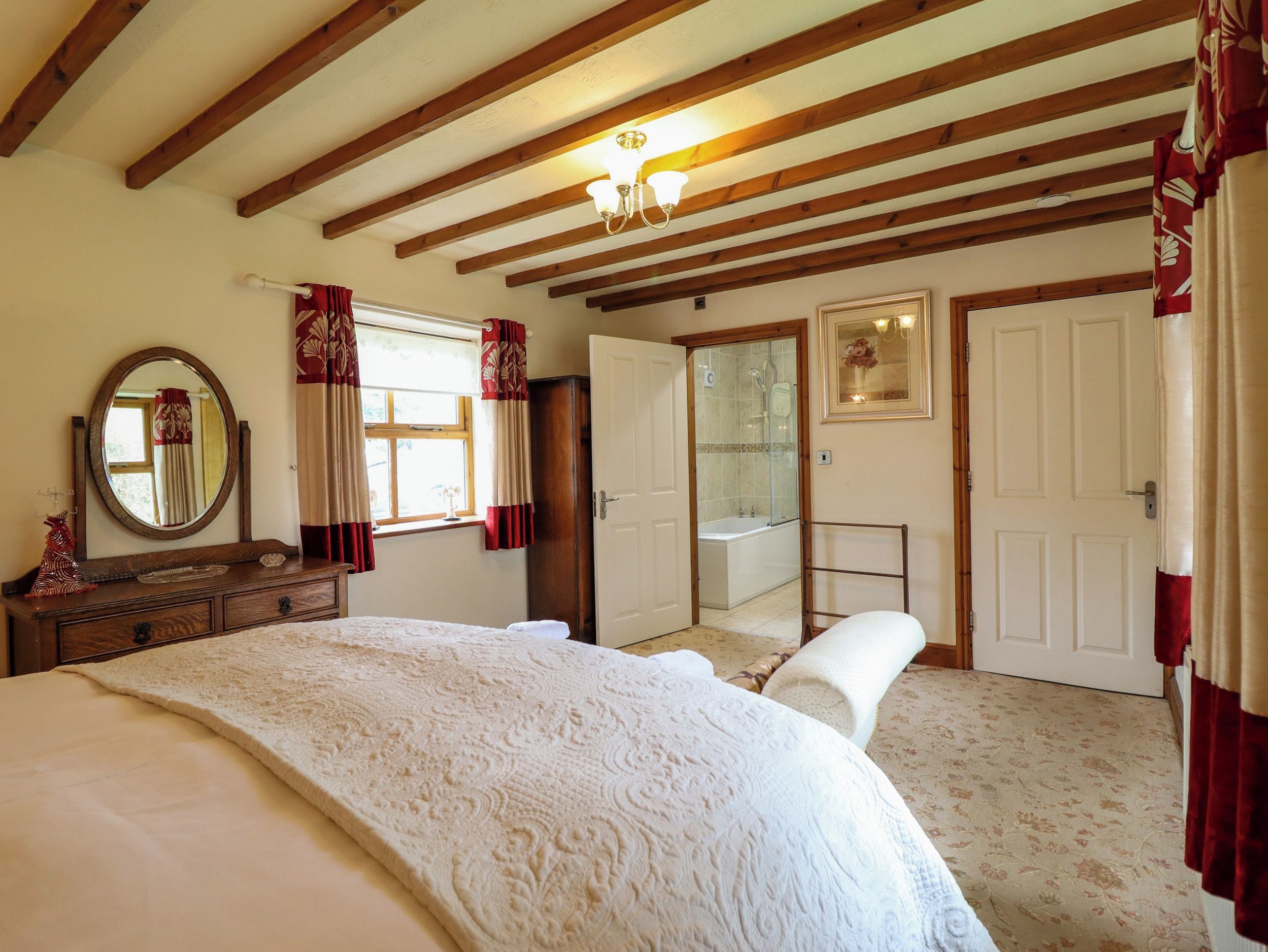 A bedroom with a large bed, a dresser, a mirror, a wardrobe, and a bathroom with a bathtub.