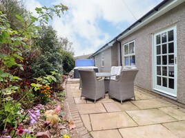 A patio with wicker furniture, a stone pathway, and a building with a window and door.