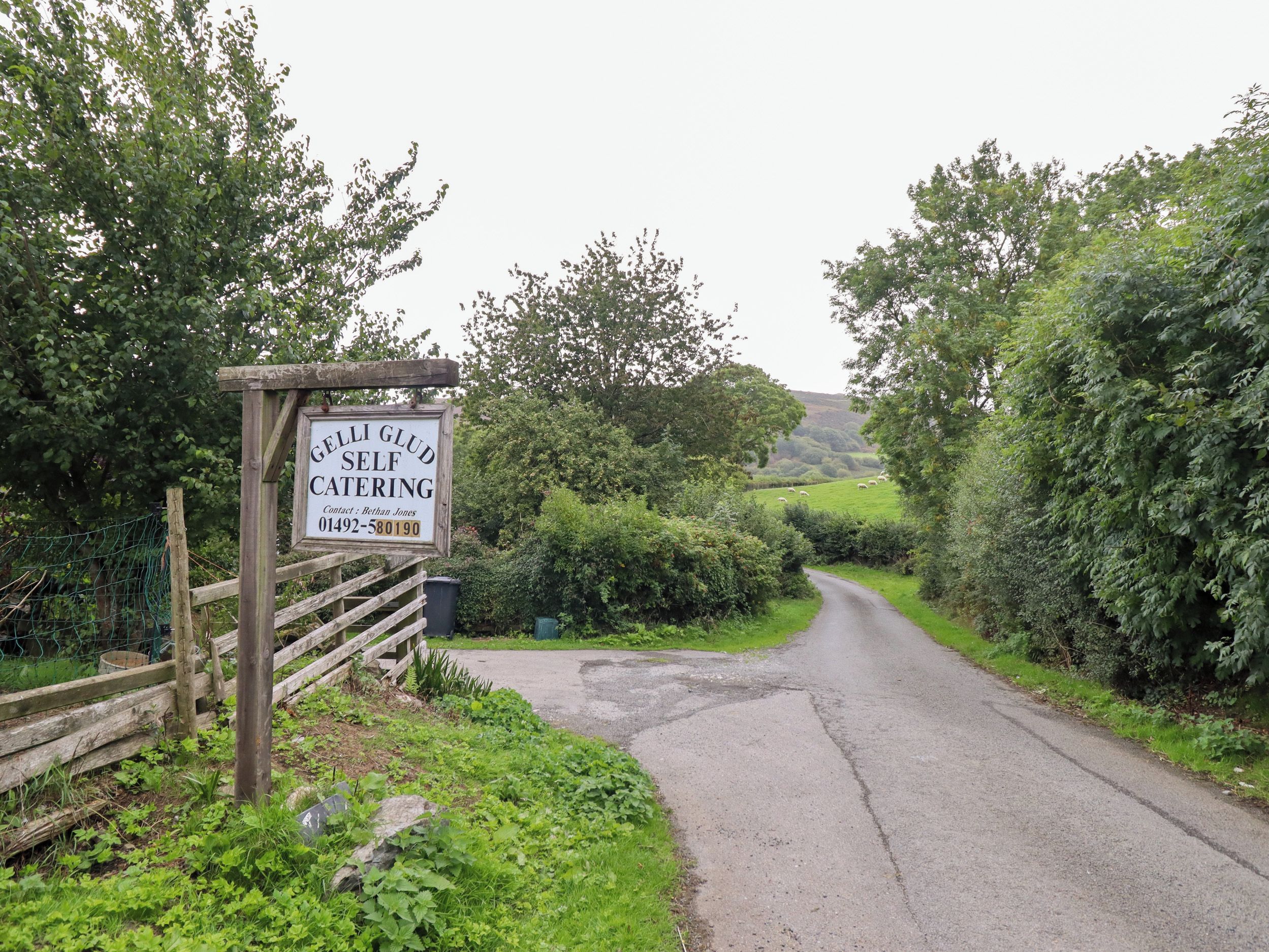 Un camino rural que conduce a un cartel que indica una cabaña rural con servicios incluidos llamada 'Gelli Glud'.