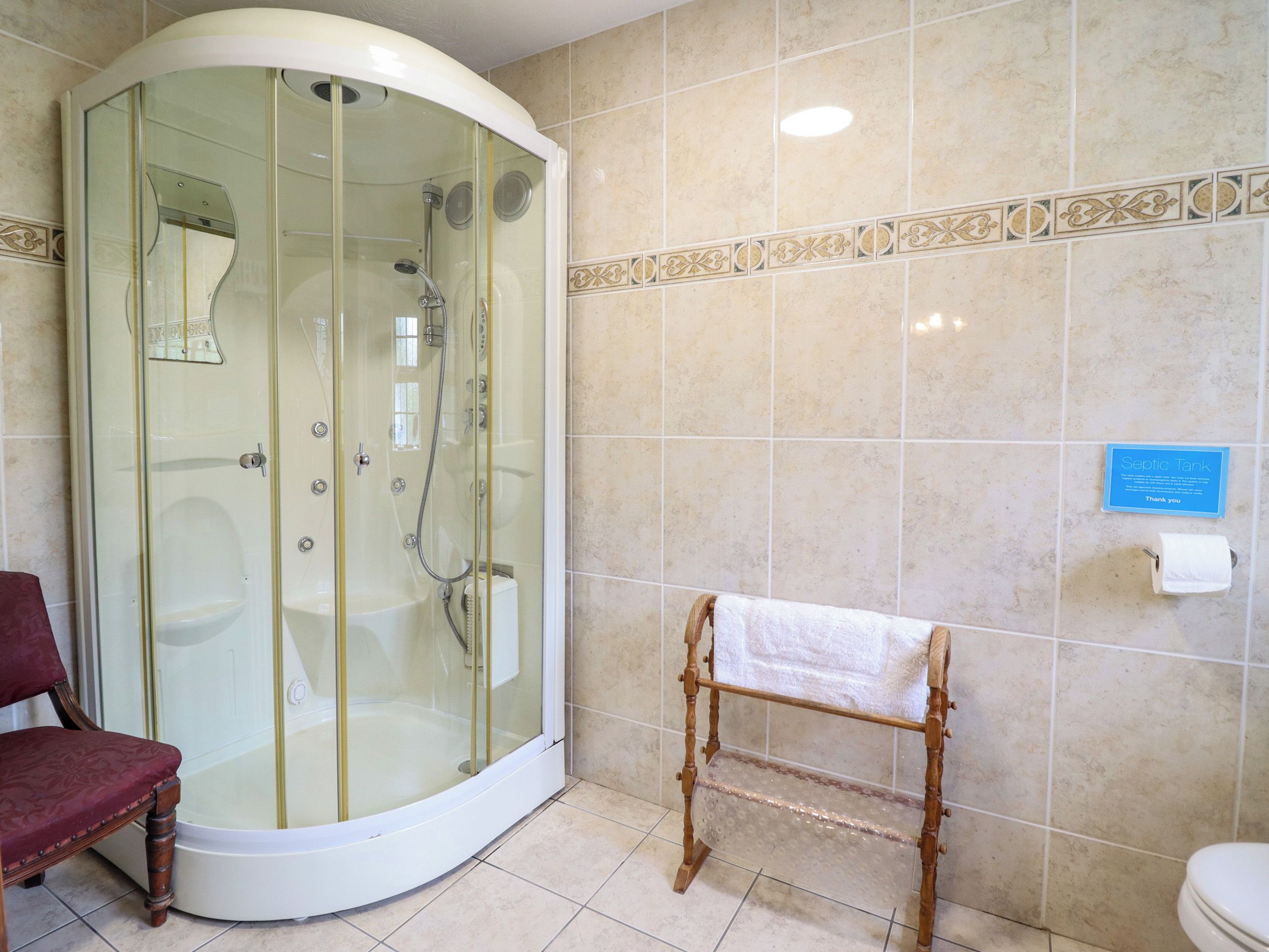 Un baño con ducha de vidrio, banca de madera, inodoro y un cartel que indica un sistema séptico.