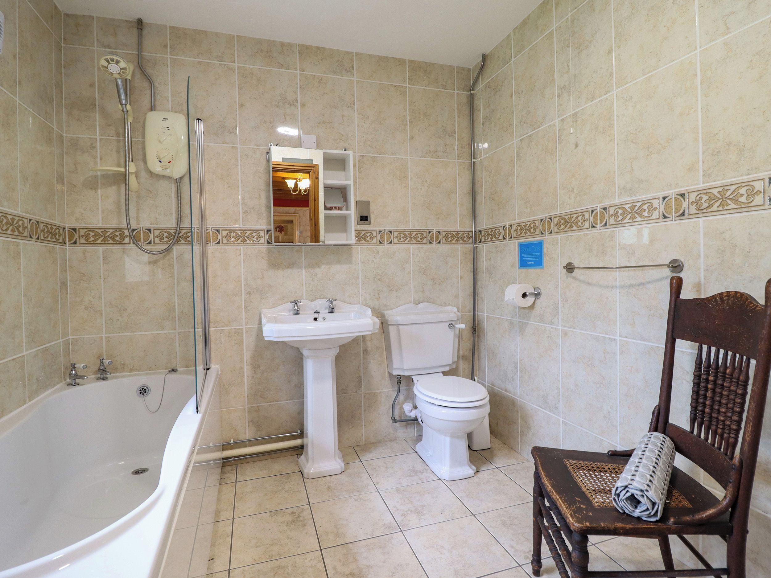 A bathroom with a bathtub, sink, toilet, and a wooden chair.