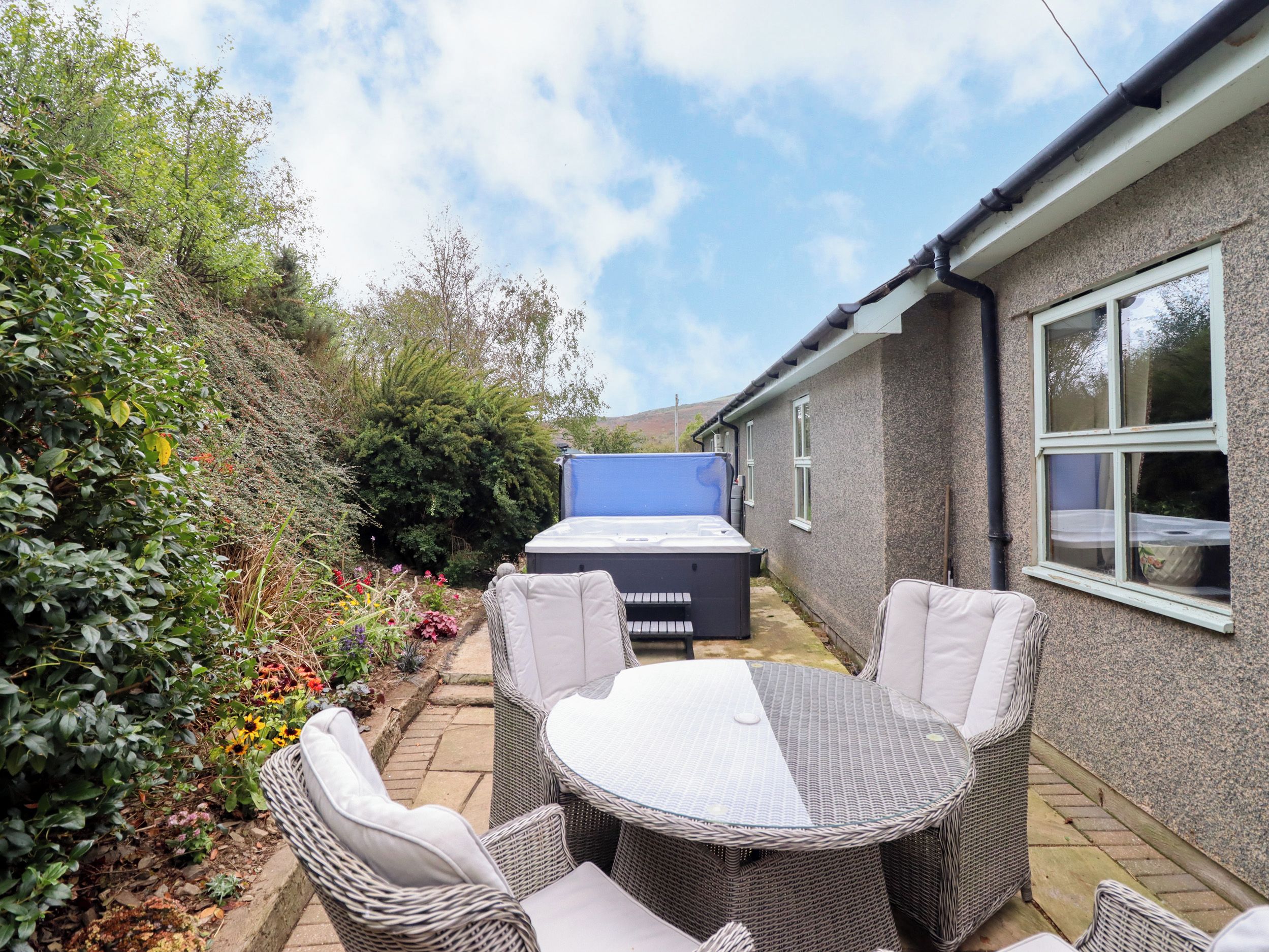 Een terras buiten met rieten meubilair, een jacuzzi en een tuin.