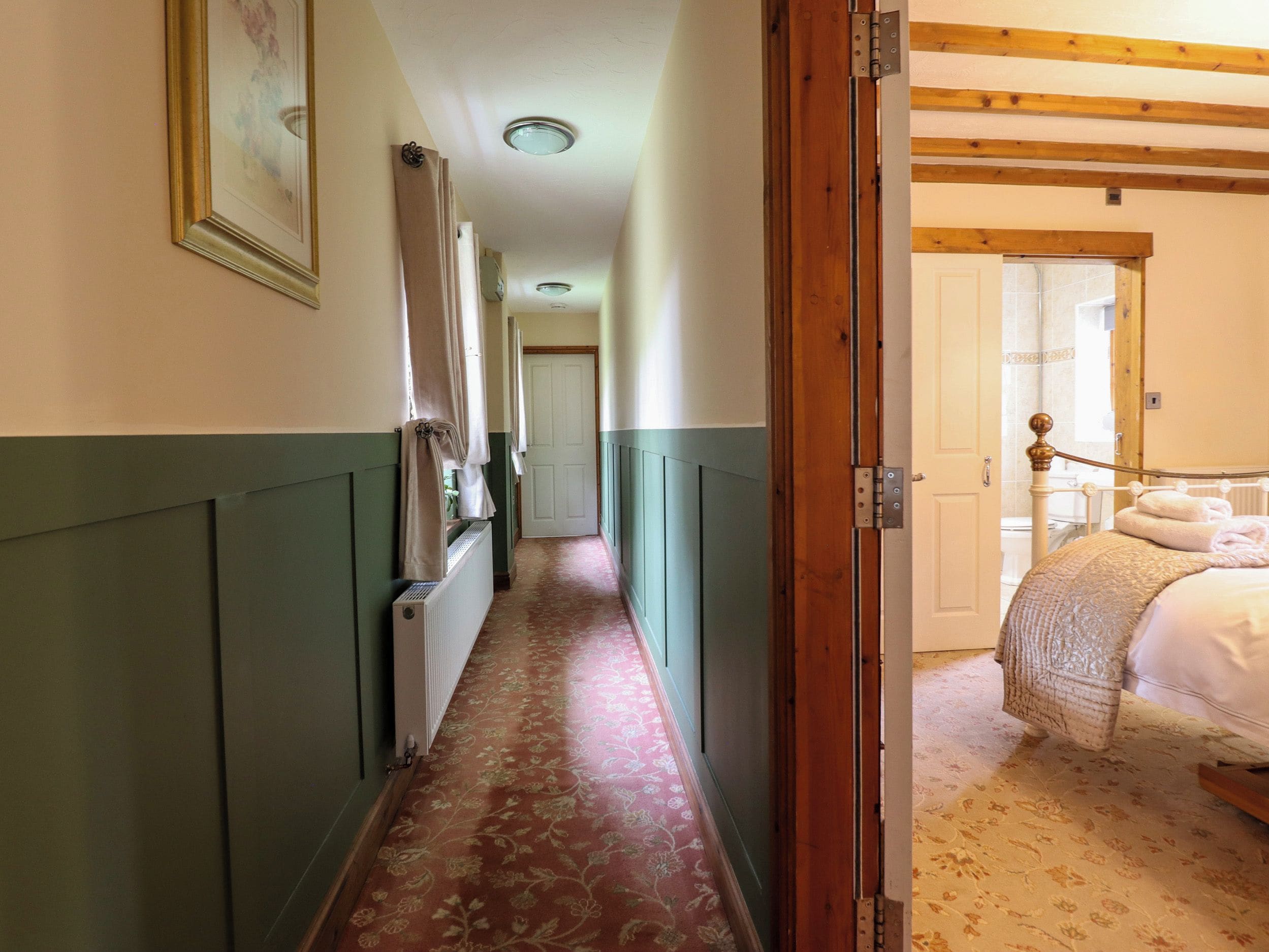 A hallway with a radiator, a bed with a wooden headboard, and a door leading to a bathroom.