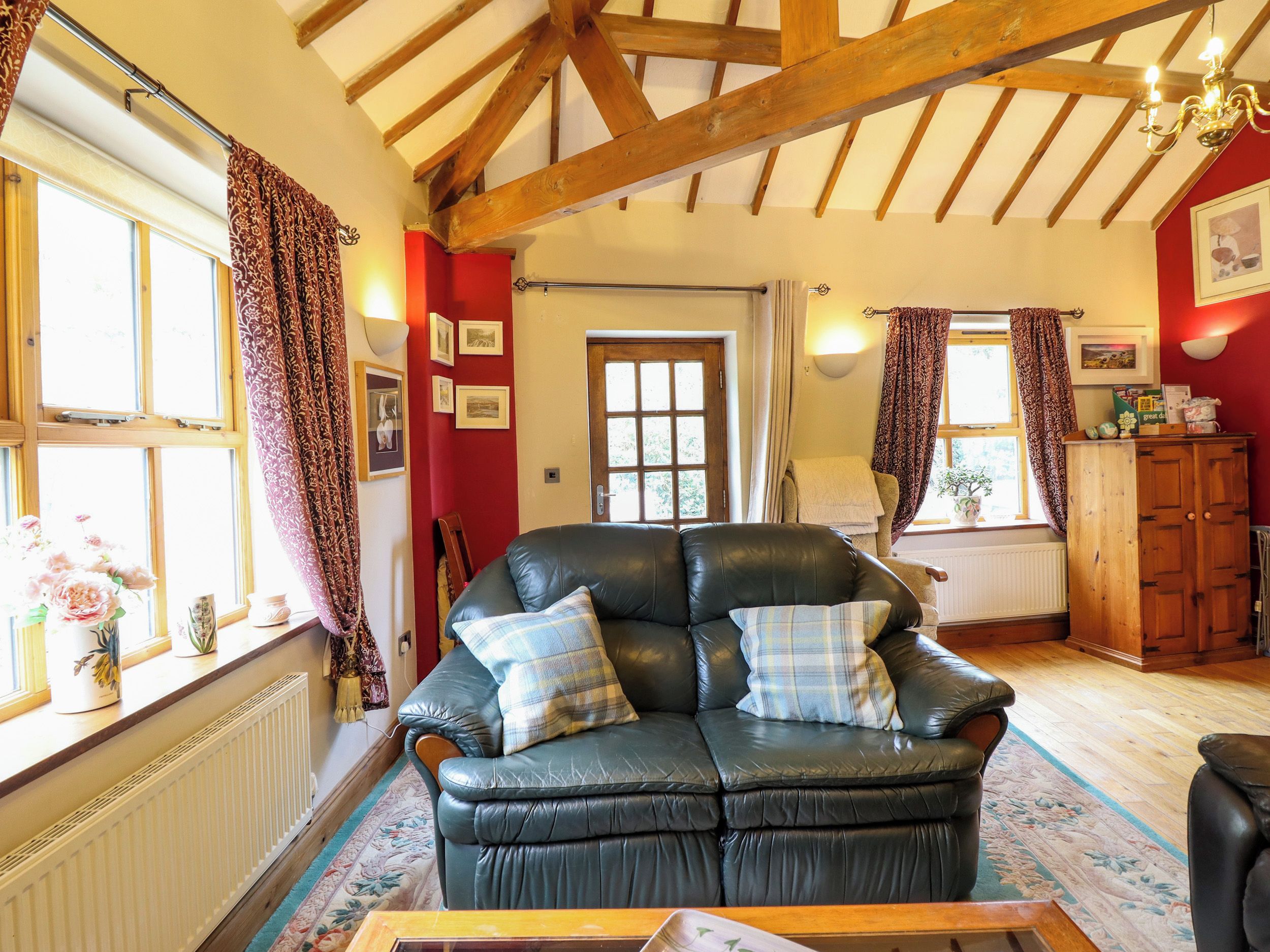 A cozy living room with a leather sofa, wooden beams, and a radiator.