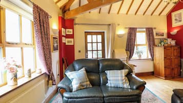 A cozy living room with a leather sofa, wooden beams, and a radiator.