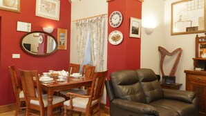A dining area with a wooden table set for four, surrounded by wooden chairs. A brown leather sofa is positioned in front of the table. - Gelli Glud (Colwyn Bay)