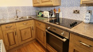 A kitchen with wooden cabinets, a stainless steel sink, a built-in oven, and a tiled backsplash. - Gelli Glud (Colwyn Bay)