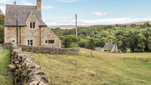 Une maison en pierre avec un toit en pente, une cheminée et un mur de pierre à l’avant.