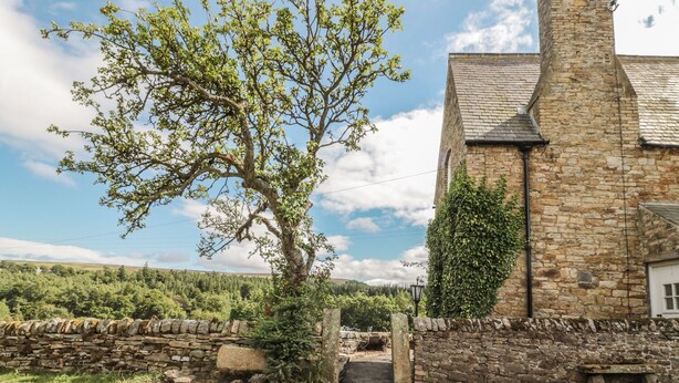 Un bâtiment en pierre à l’architecture traditionnelle, avec un arbre devant et un mur en pierre.