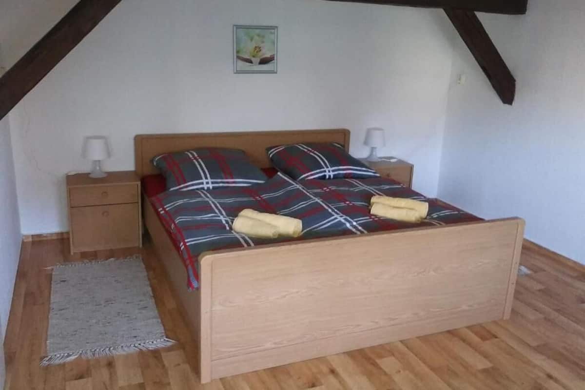 A bedroom with a wooden bed, plaid bedding, two bedside tables with lamps, a small rug, and a picture on the wall.