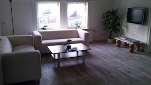 A living room with a sofa, a coffee table, a TV, and a plant. - Ferienwohnung Langelsheim (Langelsheim)