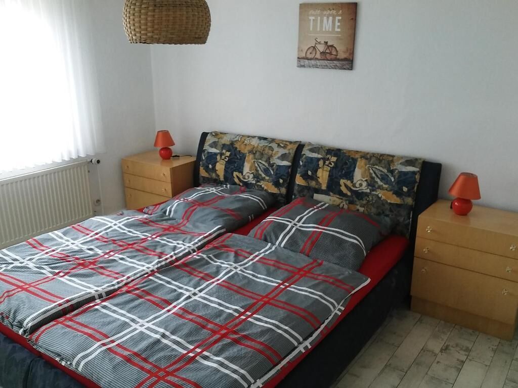 Een slaapkamer met een bed, twee nachtkastjes, een lamp, een radiator en een muur met een poster.