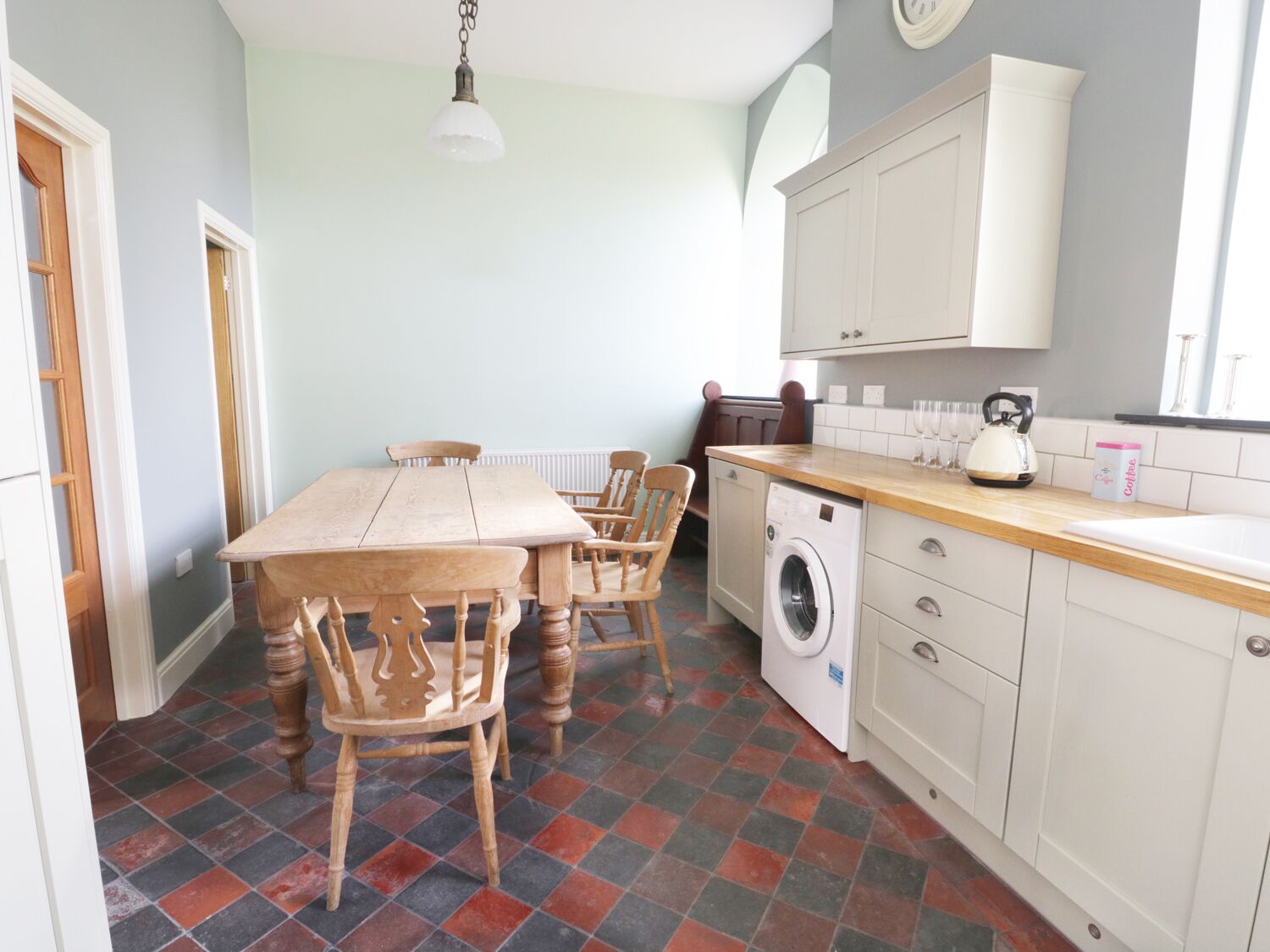 A compact kitchen with a dining table, chairs, a washing machine, and a kettle.