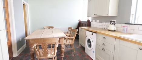 A compact kitchen with a dining table, chairs, a washing machine, and a kettle.