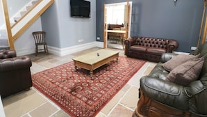 A living room with a staircase, a television, a brown leather sofa, a wooden coffee table, and a patterned rug. - No 1 Church Cottages (Llanelli)