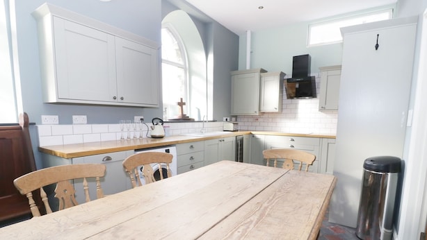 A kitchen with a wooden table, two chairs, a sink, and a stove. - No 1 Church Cottages (Llanelli)