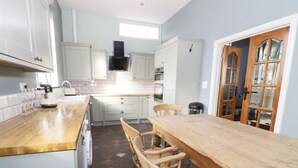 A kitchen with white cabinets, a wooden dining table, and a window. - No 1 Church Cottages (Llanelli)
