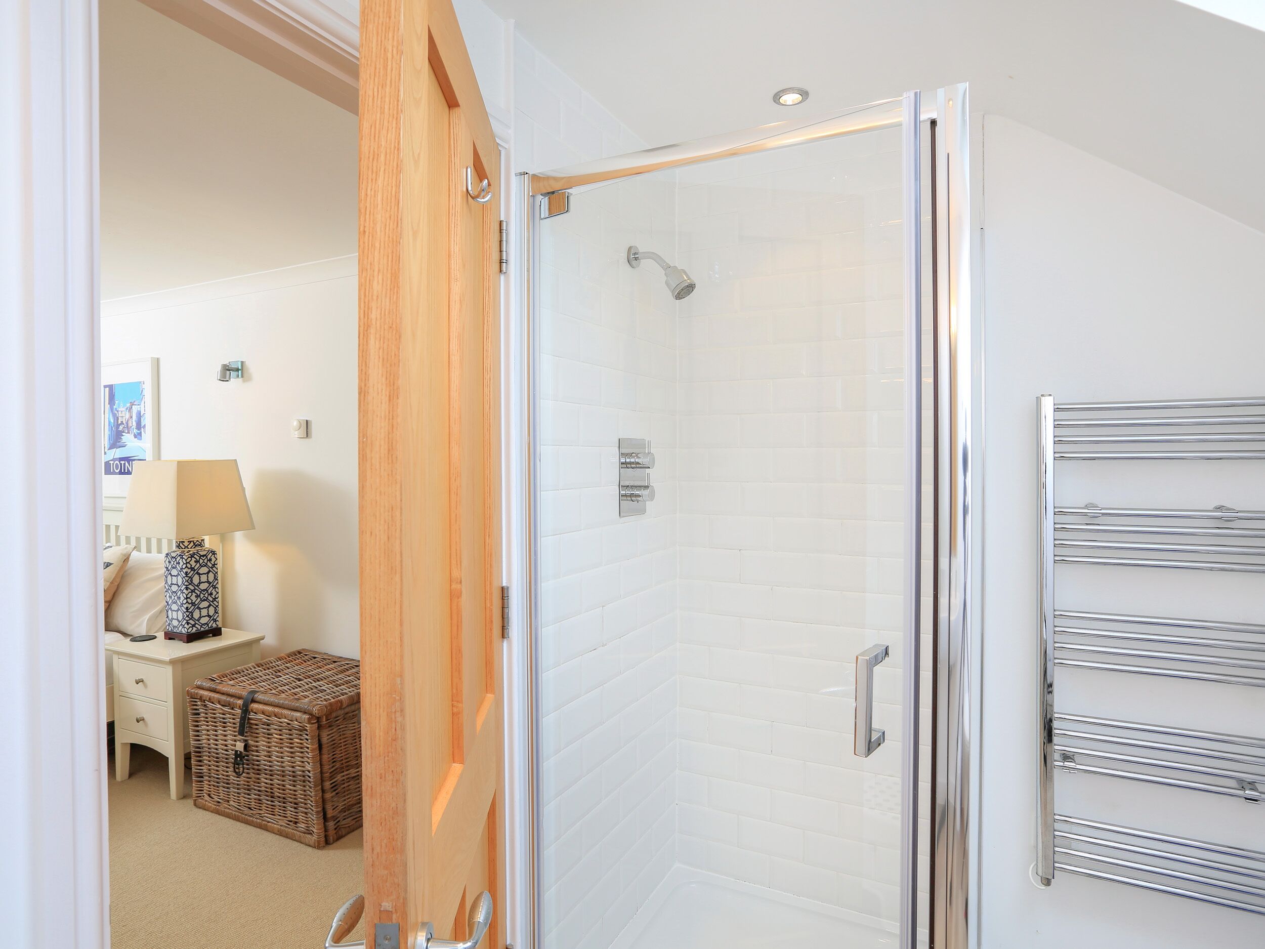 A modern bathroom with a glass shower enclosure, a white tiled wall, and a towel rack.