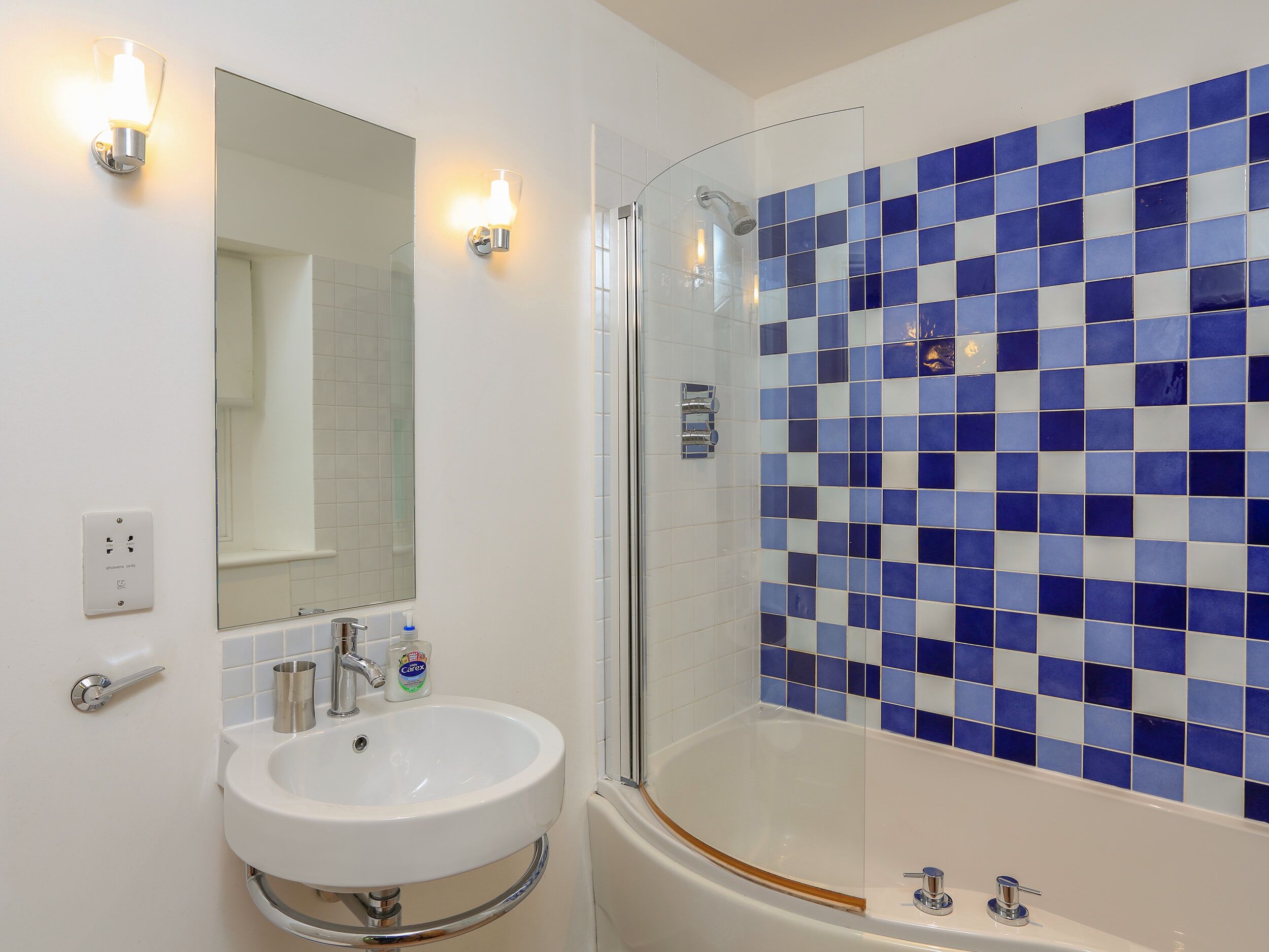 A bathroom with a white sink, a glass shower enclosure, and a blue-tiled wall.