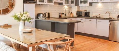 A modern kitchen with a glass dining table, wooden chairs, and stainless steel appliances.
