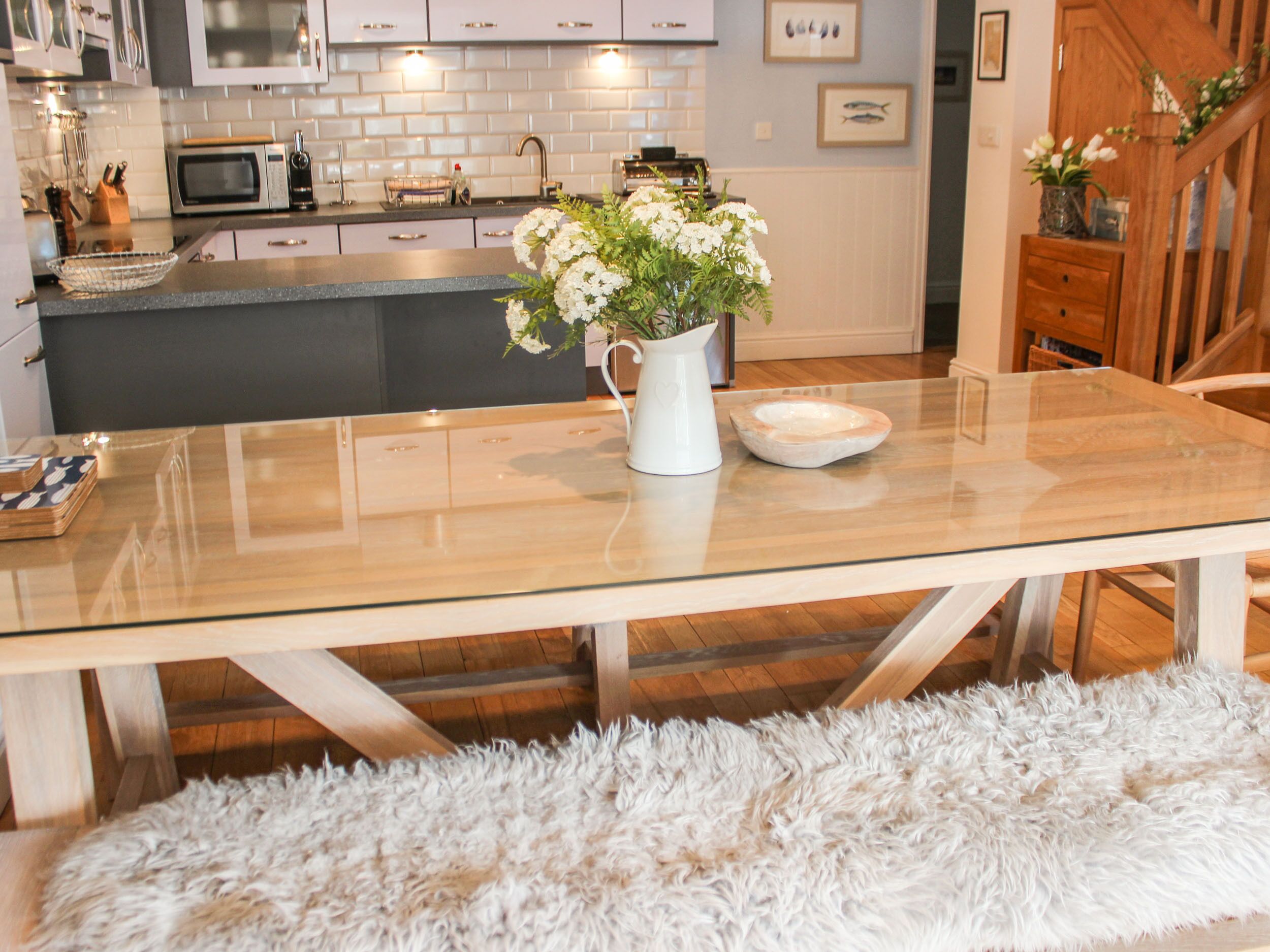 A modern kitchen with a glass-top dining table, white flowers, and wooden cabinets.