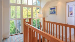 Una habitación amplia con ventanas grandes, una escalera de madera y vistas al verdor exterior.