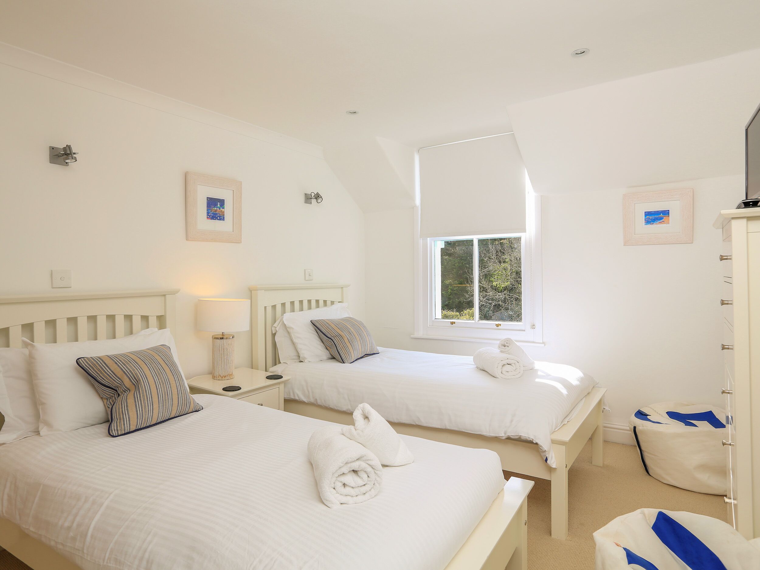 Habitación de hotel con dos camas, una ventana, un armario y una mesita con lámpara.