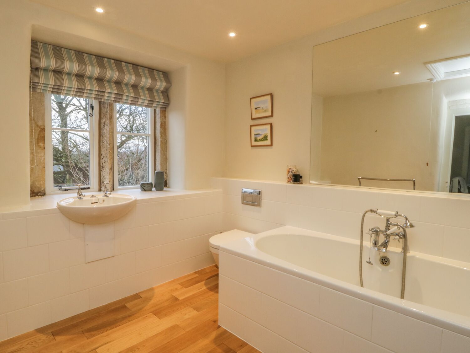 A bathroom with a large bathtub, a sink, and a window with a striped valance.