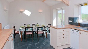 A kitchen with a dining area, wooden beams, a dishwasher, and a window with a view.
