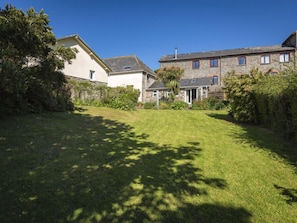 A residential property with a well-maintained lawn, stone and brick buildings, and mature trees providing shade.